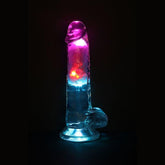 The RealRock Wireless Rechargeable LED Vibrating With Balls 7" by Shots America glows with colorful pink, blue, and red lights from within, lighting up its transparent, phallic-shaped design against a dark background.
